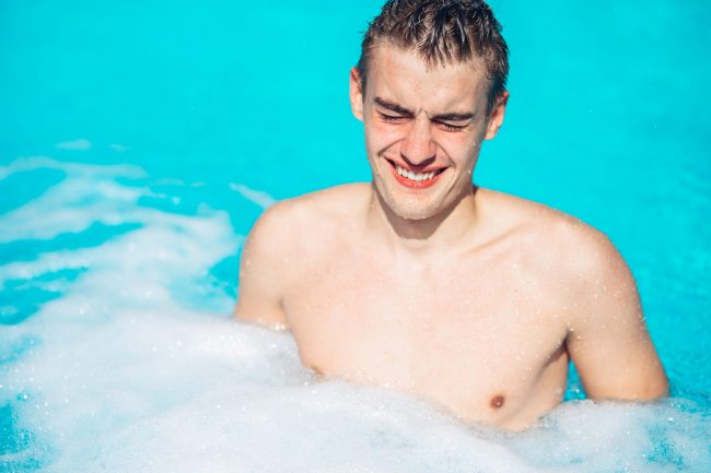 Young man rubbing eyes in swimming pool.Summer activity.Contact lens pollution, swimming in chlorine contaminated pool.Eyes burning in the pool.Allergy on chlorine chemical disinfection in water.